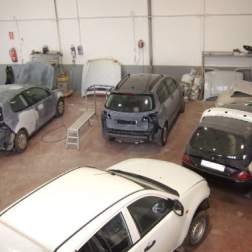 Interior de nave grande con varios coches en reparación