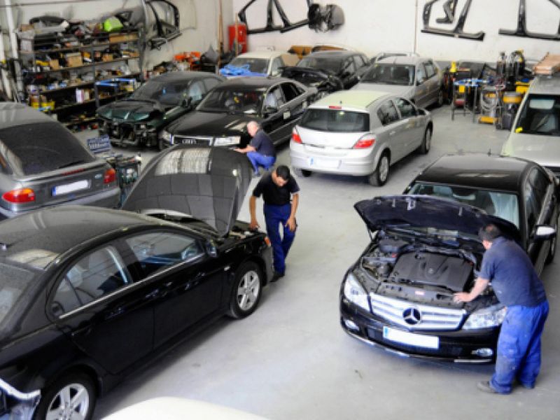 Varios coches y mecánicos en interior de nave grande